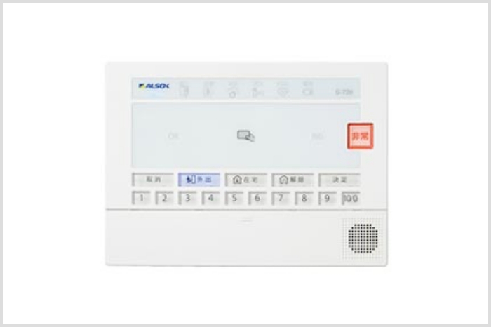壁に設置するタイプの長方形の機器。色は白。非常用のボタンやカードをかざす部分、数字入力用のパネルがついている。