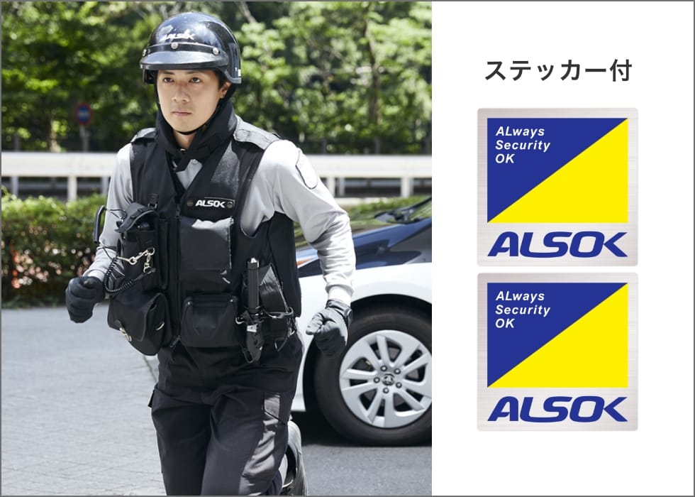 制服を着たALSOKのガードマン（警備員）が駆け寄ってくる様子の写真。写真の右側には、ステッカー付の文字。その下に、ALSOKのステッカーが二枚並んでいる。